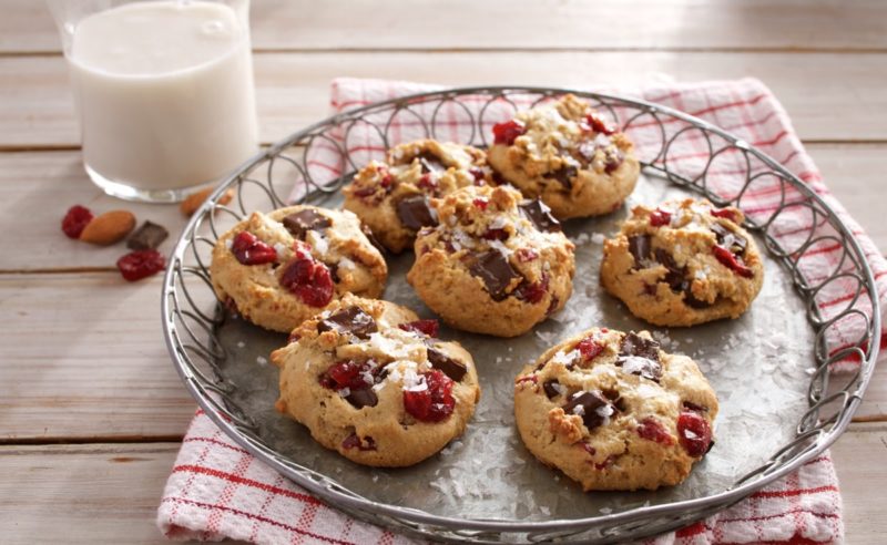 Seven bittersweet chocolate chunk cranberry cookies with a glass of liquid on the side